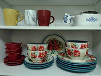 Photo of two shelves holding a set of floral stoneware dishes, mugs in different colors, and a white butter dish with blue floral pattern.