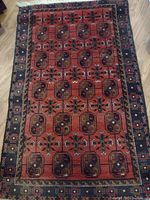 Full view of rectangular red and black wool rug showing overall pattern and natural fringe