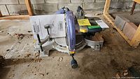 Full view of the compound mitre saw showing the angle scale, handle, and dust collection bag.