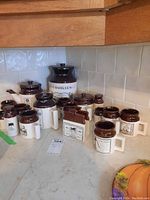 Group shot of all pieces on countertop showing arrangement of cookie jar, pots, mugs, napkin holder and shakers