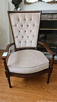 Front view of wood framed armchair with beige upholstery, showing tufted backrest and padded seat cushion.