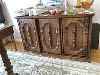Full front view of Bassett furniture sideboard showing three cabinet doors with decorative vertical handles, wood grain finish, and ornamental metal corner details