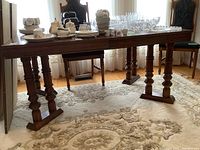 Full side view of the rectangular Bassett dining table with items on top (contents not included). Shows wooden finish and turned legs extending the table length.