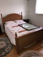 Full view of assembled wooden bed frame with mattress, floral bedding, and a framed mirror placed on the bed.