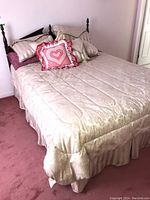 Queen size bed fully made with decorative pillows and beige comforter, showing entire bed and carpeted floor.