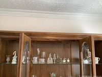 Closed wood cabinet with glass shelves holding various figurines, glassware, and dishes.