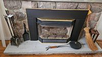 Full view of fireplace with stone backdrop showing all fireplace tools, shovels, poker, picker, brooms, popcorn maker, and candle lantern on and around the hearth.