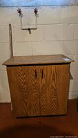 Front view of wooden fish tank cabinet stand with two doors and black handles placed against concrete block wall.