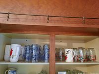 Shelf view showing assorted glassware with floral and Christmas patterns and ceramic holiday mugs.