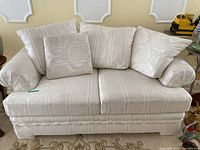 Front view of cream patterned loveseat with 5 matching cushions arranged on seat and arms.