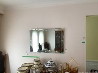Full view of the rectangular bevelled wall mirror hanging on a wall above a dining table with various decorative items reflected and nearby.