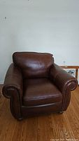 Front right angle view of brown leather armchair showing rolled arm and nailhead trim