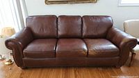 Front view of brown leather three-seat sofa on wood floor