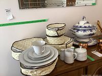 Overview photo showing china on wood surface with protective storage cases stacked behind. Includes cups, plates, cream, sugar, and salt and pepper shakers.
