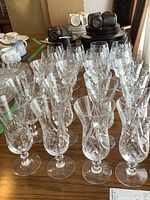 Photo showing a large arrangement of clear crystal stemmed glasses with detailed pinwheel cut pattern on a wooden table.