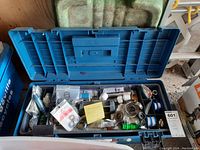 Blue plastic tool box open showing assortment of plumbing tools and parts including sealed small parts bags, rubber gaskets, and coiled springs.