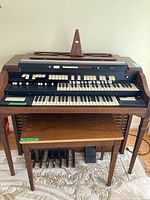 Full front view of the Rhythm II electric organ showing double keyboard, control panel, wooden casing, and matching stool underneath with pedal assembly visible.