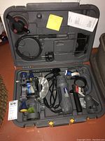 Full view inside the carrying case showing the spin saw with multiple attachments and manuals.