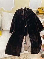 Full view of dark brown fur coat on hanger with belt and scarf draped