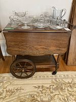 Full view of the wooden tea cart with glassware on top, showing the extendable wooden ends and floral carvings.
