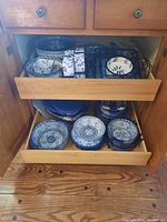 Two wooden drawers open showing the full assortment of ceramic dishes and metal trays.