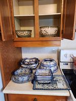Ceramic serving bowls, plates, dishes, and a serving tray featuring blue and white floral motifs on countertop and cabinet shelves