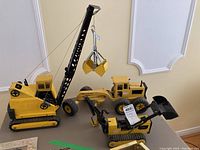 Overview of three vintage Tonka steel construction vehicles: dragline crane, road grader, tracked front loader.
