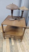 The two flying saucer mushroom desk lamps placed on top of the wooden side table showing overall condition.