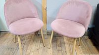 Front view of one pink upholstered modern chair showing seat and backrest with wooden legs on wood floor.