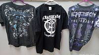 Three vintage concert T-shirts hanging: DarkStar, Acrassicauda, Excision The Paradox tour shirt