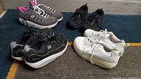 Four pairs of Skechers Shape-Ups tennis shoes arranged on floor, showing colors and condition.