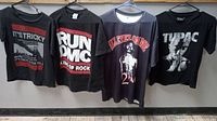 Four t-shirts hung in a row showing the front side, featuring two RUN DMC shirts and two Tupac Shakur shirts.