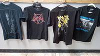 Four vintage T-shirts hanging on a rod: Tupac Shakur praying, Slayer band logo, Boyz in the Hood graphic, Beastie Boys Check Your Head.