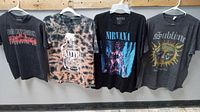 Four vintage rock band T-shirts hanging on hangers, front view showing logos and graphics clearly.