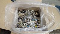 View inside the USPS Priority Mail box showing a large quantity of mixed vintage jewelry pieces including bracelets, rings, earrings, and brooches mostly silver-tone with some colored accents.