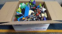 Large USPS Priority Mail box open showing mixed LEGO pieces inside, notable various colors and large quantity.