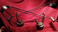 Two black metal balance desk lamps with adjustable arms and weighted bases on a red fabric background.