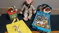Full view of all items: Pink Panther plush, Bugs Bunny jack-in-the-box, yellow Bugs Bunny tote bag, and Scooby-Doo pinball machine toy on blue carpet