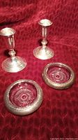 Two sterling silver candle holders and two matching ashtrays arranged on a red textured cloth background, showing the overall set and condition.