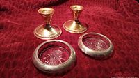 Photo showing two sterling silver candle holders with wide bases and two matching ashtrays with silver rims and starburst glass centers on red fabric background.