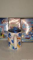 Front view showing three Lilo & Stitch DVD movie cases arranged side by side with the Disney Lilo & Stitch ceramic mug in front.