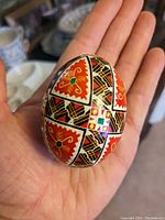 Close-up photo of one hand-painted Ukrainian egg showing detailed geometric and floral patterns in red, black, white, green, and orange.