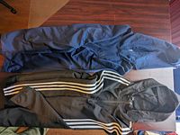 Photo showing two Adidas hooded sweatshirts, one navy blue and one black with white stripes on sleeves.