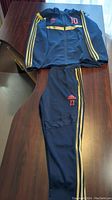 Top view of Adidas Predator two-piece navy and gold track suit laid on table