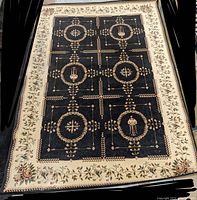 Full view of the rectangular area rug showing black patterned center and floral cream border.
