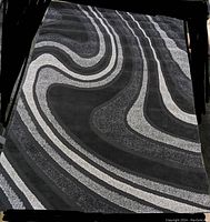 Full view of the black and gray area rug showing abstract wavy striped design