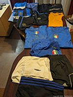 Top-down view of athletic wear including jerseys, shirts, shorts and track pants spread on table, showing colors and logos