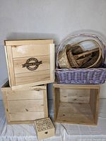 Photo of three wooden boxes stacked and a collection of various baskets in a purple wicker basket, plus small decorative wooden box in front.