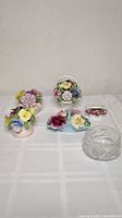Image showing five porcelain floral figurines including basket shapes, a vase with flowers, a floral spray, and a clear glass dish on a white cloth background.