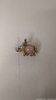 Gold tone elephant brooch with a clear cabochon belly on a white background, showing detail and condition.